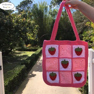 May include: Pink and white crocheted tote bag with strawberry appliques. The bag has a square shape and two straps.