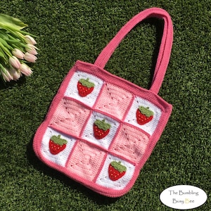 May include: Pink and white crocheted tote bag with strawberry appliques. The bag has two straps and a square shape. The text "The Bumbling Busy Bee" is visible in the bottom right corner.