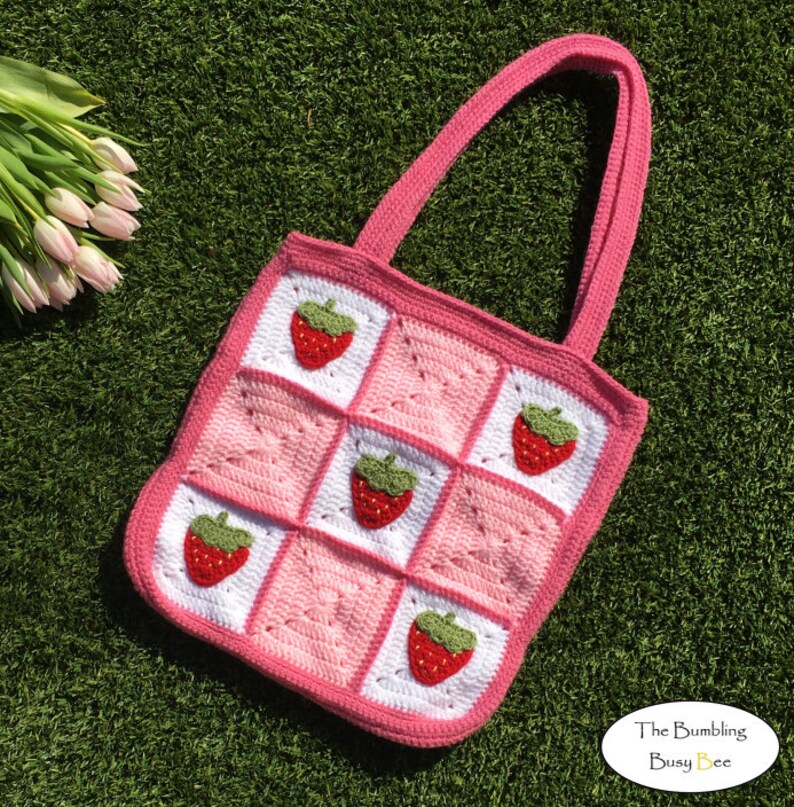 May include: Pink and white crocheted tote bag with strawberry appliques. The bag has two straps and a square shape. The text "The Bumbling Busy Bee" is visible in the bottom right corner.