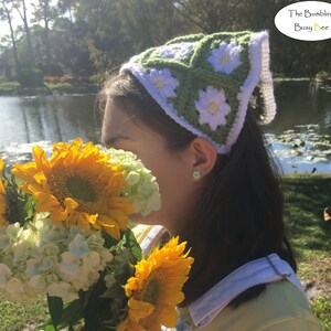 May include: A woman wearing a green and white crocheted headband with a daisy pattern. The headband is tied at the back of her head. She is holding a bouquet of sunflowers and white hydrangeas.