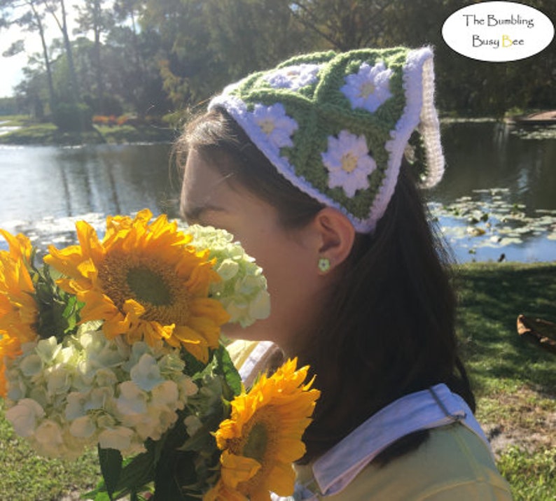 May include: A woman wearing a green and white crocheted headband with a daisy pattern. The headband is tied at the back of her head. She is holding a bouquet of sunflowers and white hydrangeas.