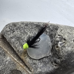 May include: A black and green fly fishing lure with a bright yellow head.