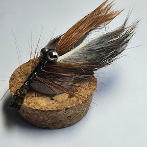 May include: A brown, white, and gray fly fishing lure with a bead head and a green and black body.