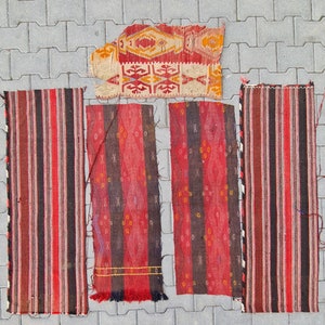 May include: Five vintage Turkish rugs with red, black, and white stripes and geometric patterns. The rugs are laid out on a gray concrete surface.