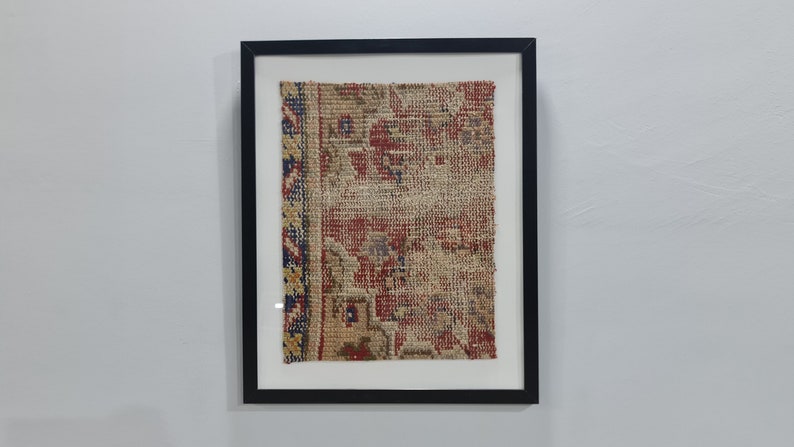 May include: A framed piece of antique fabric with a red, blue, and yellow pattern. The fabric is woven with a geometric design and has a worn, vintage look.