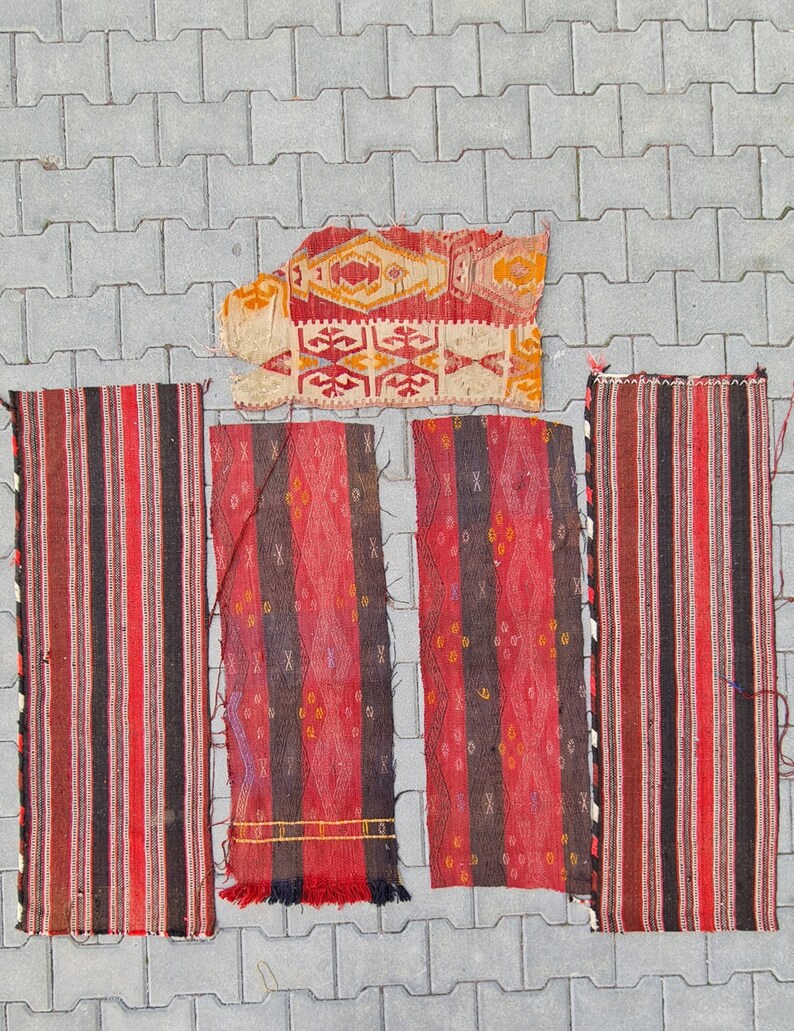 May include: Five vintage Turkish rugs with red, black, and white stripes and geometric patterns. The rugs are laid out on a gray concrete surface.