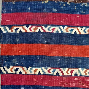 K&ouml;nnte beinhalten: Nahaufnahme eines gewebten Stoffes mit einem gestreiften Muster in Blaut&ouml;nen, Rot und Braun. Der Stoff hat eine raue Textur und ein leicht verblichenes Aussehen.