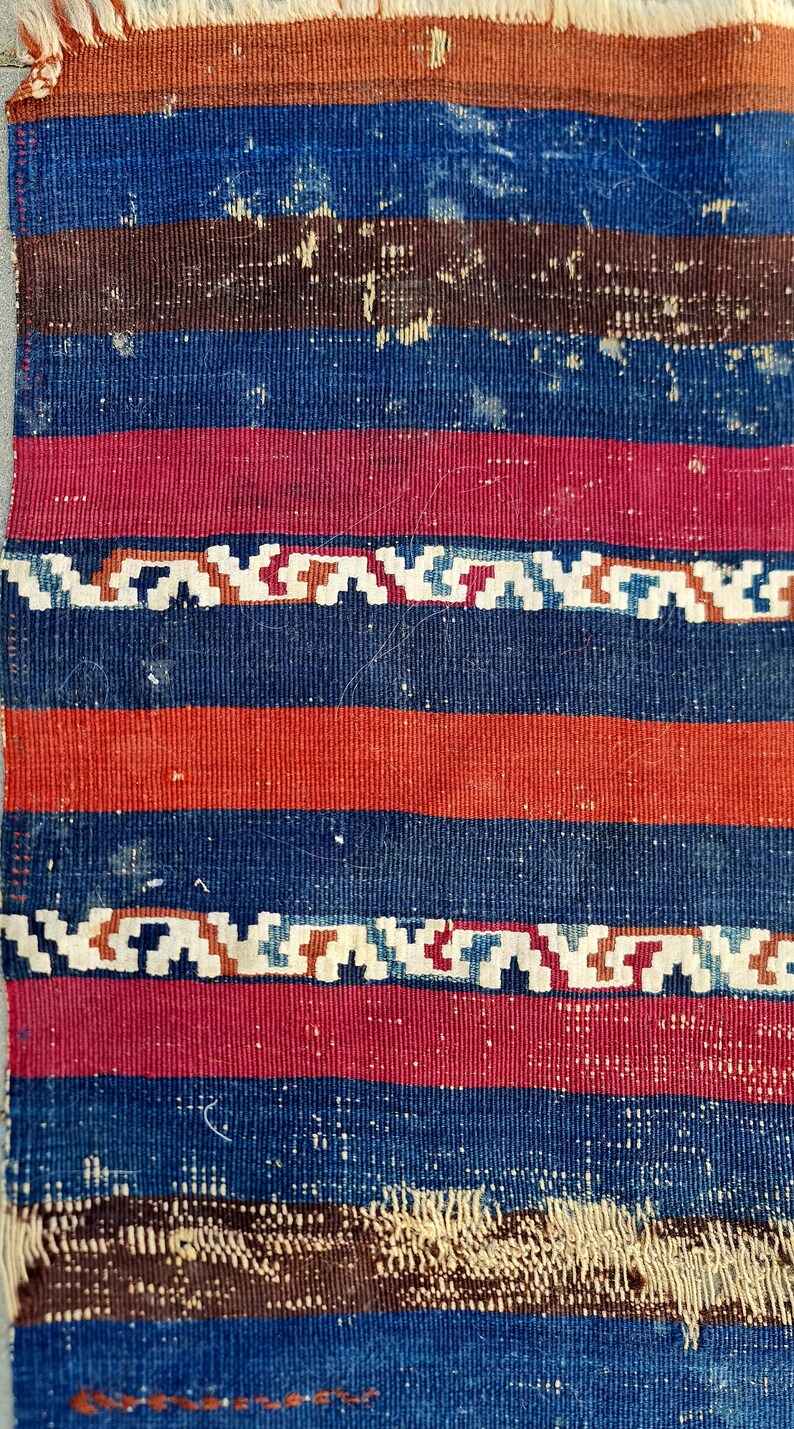 K&ouml;nnte beinhalten: Nahaufnahme eines gewebten Stoffes mit einem gestreiften Muster in Blaut&ouml;nen, Rot und Braun. Der Stoff hat eine raue Textur und ein leicht verblichenes Aussehen.