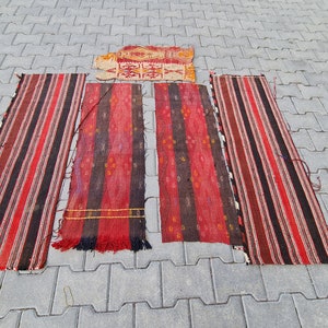 May include: Five red, black, and white striped rugs laid out on a gray concrete surface. The rugs are all different lengths and widths.