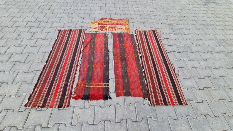 May include: Five red, black, and white striped rugs laid out on a gray concrete surface. The rugs are all different lengths and widths.