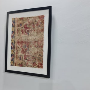 May include: A framed piece of antique fabric with a faded floral pattern in shades of red, blue, and yellow. The fabric is displayed on a white background.