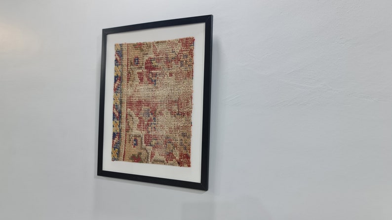 May include: A framed piece of antique fabric with a faded floral pattern in shades of red, blue, and yellow. The fabric is displayed on a white background.