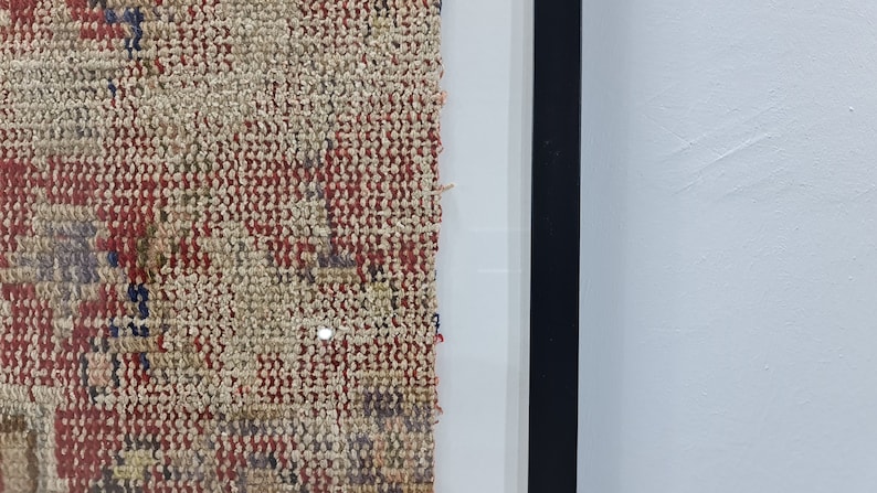 May include: Close-up of a framed piece of woven fabric with a red, white, and blue pattern. The fabric is frayed on the edges and has a textured surface.