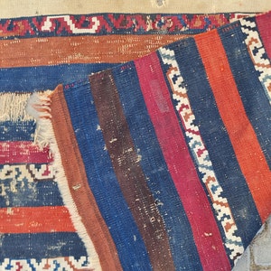 K&ouml;nnte beinhalten: Ein Vintage-Streifen-Teppich mit ausgefransten R&auml;ndern. Der Teppich ist aus Wolle und hat eine Vielzahl von Farben, darunter Rot, Blau, Braun und Wei&szlig;.