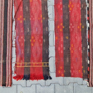May include: Four red, black, and white striped woven rugs with fringe. The rugs have different patterns and are laid out on a gray concrete surface.