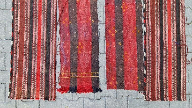 May include: Four red, black, and white striped woven rugs with fringe. The rugs have different patterns and are laid out on a gray concrete surface.