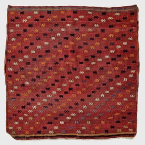 May include: A rectangular, hand-woven rug with a red background and a repeating pattern of small, colorful cross-like motifs. The motifs are in shades of yellow, black, white, and blue. The rug has a border with a dark stripe.
