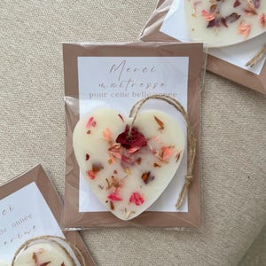 Peut inclure: Un ornement en cire blanche en forme de cœur incrusté de pétales de fleurs séchées roses, rouges et orange. Il est suspendu par une boucle en ficelle brune et emballé dans un sachet plastique transparent sur une carte avec le texte Merci maîtresse pour cette belle année.