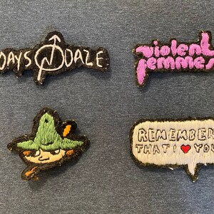 Puede incluir: Cuatro parches bordados, dos con los nombres de las bandas "Days Daze" y "Violent Femmes", uno con un personaje de dibujos animados con un sombrero verde y otro con un bocadillo que dice "Recuerda que te quiero".