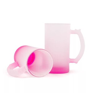 May include: Two pink frosted glass mugs with a gradient from white to pink. The mugs have a handle and are perfect for drinking beverages.