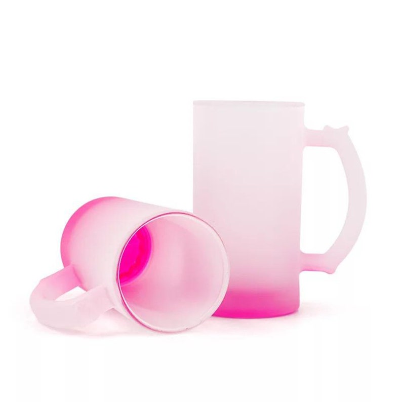 May include: Two pink frosted glass mugs with a gradient from white to pink. The mugs have a handle and are perfect for drinking beverages.