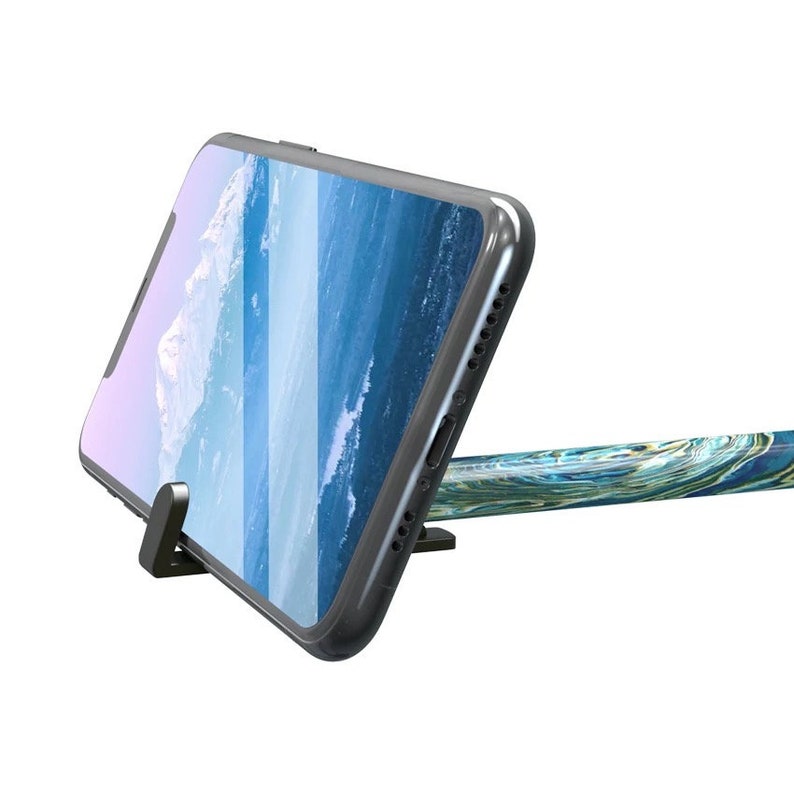 May include: A black smartphone is propped up on a black stand. The phone displays a blue and white ocean scene. A patterned cable, with blue, green, and gold swirls, is connected to the phone.