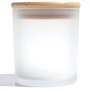 May include: A frosted glass candle jar with a wooden lid. The jar is empty and has a smooth, white finish.