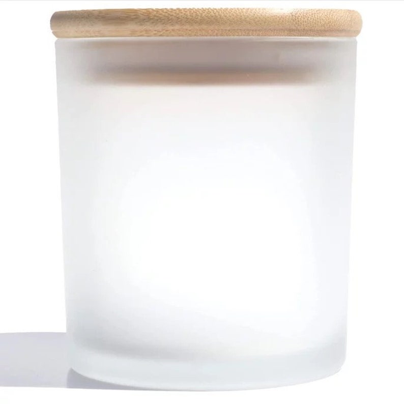 May include: A frosted glass candle jar with a wooden lid. The jar is empty and has a smooth, white finish.