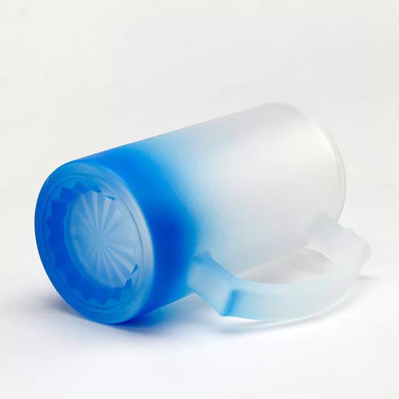May include: A frosted glass beer mug with a blue to white ombre design. The mug has a handle and a textured bottom.