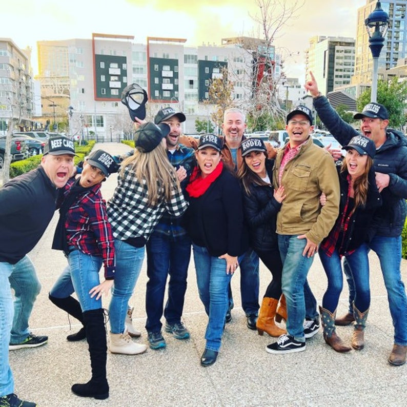 Peut inclure: Un groupe d'amis portant des casquettes de baseball noires avec des textes diff&eacute;rents. Les casquettes disent "Beef Cake", "Rodeo", "Five", et "Dark Horse". Le groupe est debout &agrave; l'ext&eacute;rieur devant un b&acirc;timent.
