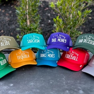May include: Ten trucker hats in various colours with embroidered text. The text on the hats reads "I'll bring the" followed by a different phrase on each hat. The phrases are "Alibi", "Sarcasm", "Bail Money", "Bad Decisions", "Tequila", "Dance Moves", "Fireball", "Voice of Reason", "Shenanigans".