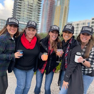 Peut inclure: Cinq femmes portant des casquettes de baseball noires avec des inscriptions diff&eacute;rentes. Les casquettes disent "They Still Call the Rodeo", "Fire & Ice", "Cowboy & Hats", "Ain't Goin Down", et "Blame it all on my Roots".
