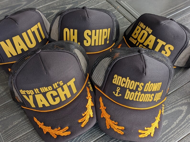 May include: Five black trucker hats with gold embroidery. The hats feature nautical themed phrases like "Nauti", "Oh Ship!" and "Anchors Down Bottoms Up!"
