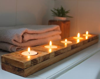 May include: A wooden candle holder with five lit tea lights. The holder is made of reclaimed wood and has a rustic finish. The candles are arranged in a row and are casting a warm glow.