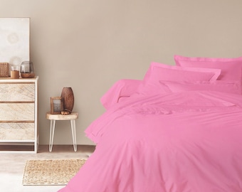 May include: A pink duvet cover and pillowcases set on a bed. The bedding is made of a soft, smooth fabric and has a simple, elegant design.