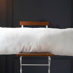 May include: A white rectangular pillow resting on a wooden chair with white metal legs against a dark gray wall.