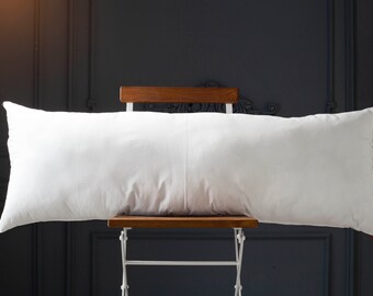 May include: A white rectangular pillow resting on a wooden chair with white metal legs against a dark gray wall.