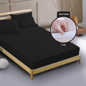 May include: Black fitted sheet with thick elastic all around. The elastic is 4 cm thick. The sheet is on a wooden bed frame.