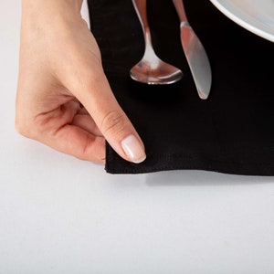 May include: A black placemat with a silver spoon and knife on top. A hand is holding the edge of the placemat.