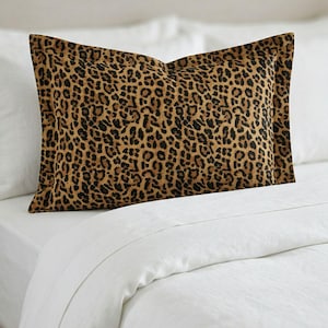 May include: A rectangular pillow with a leopard print pattern in shades of brown and black. The pillow is placed on a white bed with white sheets and a white background. The pillow is approximately 20 inches long.