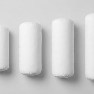 May include: Four white cylindrical pillows of varying heights are arranged on a light gray surface. The pillows are made of a soft, textured fabric and have rounded ends. The pillows are designed for comfort and support.