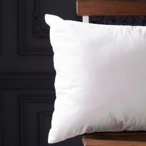 May include: A white pillow with a smooth, soft surface. The pillow is sitting on a wooden chair.
