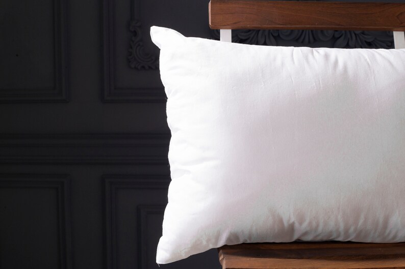 May include: A white pillow with a smooth, soft surface. The pillow is sitting on a wooden chair.