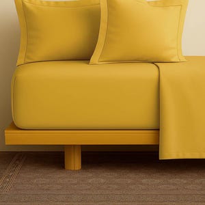 Puede incluir: Un juego de cama amarillo mostaza que incluye una sábana bajera, una sábana encimera y dos fundas de almohada. Las fundas de almohada tienen un borde decorativo. La cama está sobre un marco de madera.