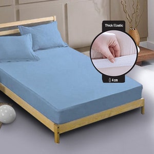 May include: A light blue fitted sheet with a thick elastic band around the edge. The elastic band is 4 cm thick. The sheet is on a wooden bed frame.