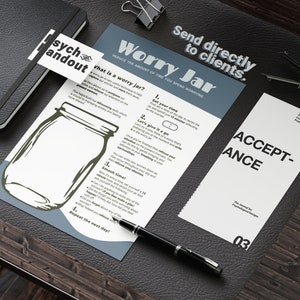 May include: A white sheet of paper with the title "Worry Jar" and instructions on how to reduce the amount of time you spend worrying. The paper is on a brown wooden surface with a black pen and a black notebook.