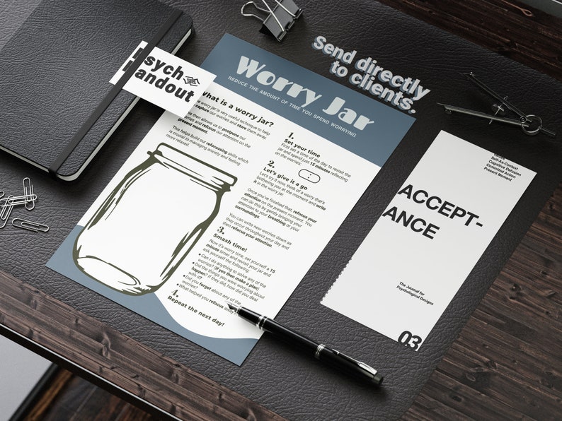 May include: A white sheet of paper with the title "Worry Jar" and instructions on how to reduce the amount of time you spend worrying. The paper is on a brown wooden surface with a black pen and a black notebook.