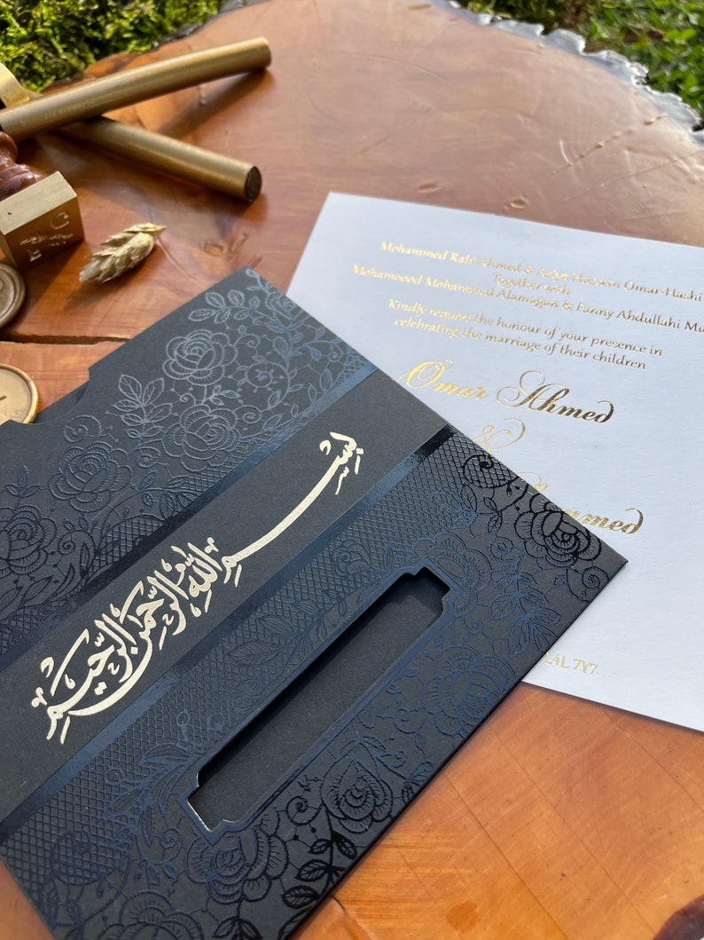 May include: A black and gold wedding invitation with an intricate floral design. The invitation features the text "Omar Ahmed" in gold lettering and the Arabic phrase "Bismillah ar-Rahman ar-Rahim" in silver lettering.