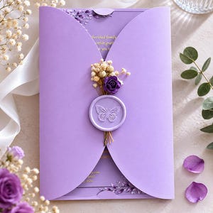 May include: A lavender invitation with a butterfly seal and floral embellishments. The invitation features a decorative butterfly seal, dried flowers, and a purple rose. The invitation is closed with a small tab and has text visible inside.