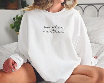 May include: A white oversized sweatshirt with the text "sweater weather" in black script.